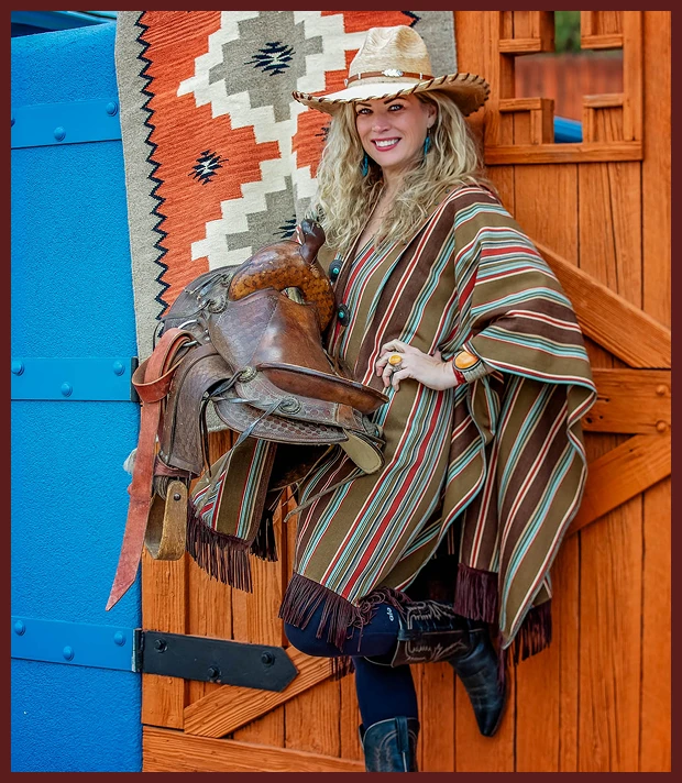 Smiling woman in cowboy hat holding saddle